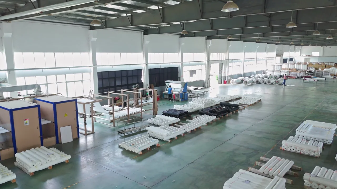 Factory production floor with pallets of white rolled material, workstations and a worker at a machine